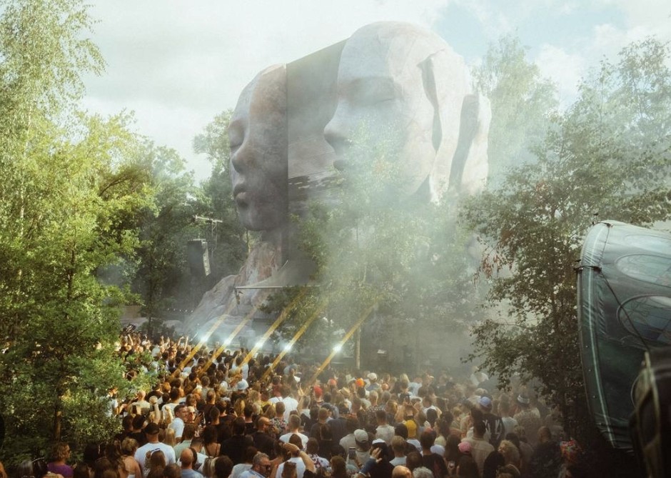 A daytime festival crowd gathered before large sculptural stage artwork